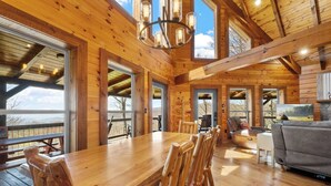 A spacious wooden interior with a large dining table, multiple chairs, a sofa, and a fireplace. - Lookout Lodge (Bryson City)
