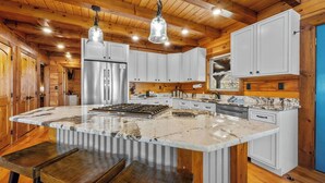 A kitchen with wooden cabinets, a large island, stainless steel appliances, and hanging pendant lights. - Lookout Lodge (Bryson City)