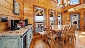 A wooden cabin interior with a dining table and chairs, a kitchen area with appliances, and large windows offering views. - Lookout Lodge (Bryson City)