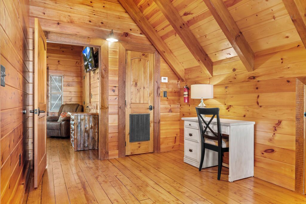 Interior de una cabaña de madera con escritorio, silla y chimenea.