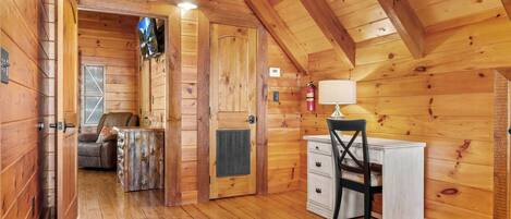 Interior de una cabaña de madera con escritorio, silla y chimenea.