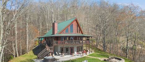 A large log cabin with a green roof, a covered porch, and a stone fireplace.