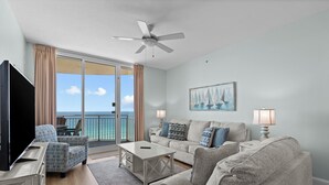 A living room with a TV, two sofas, a coffee table, and a balcony with a view of the ocean. - 2 Bedrooms in Aqua Resort - Remodeled with amazing views! Beach chairs included! (Panama City Beach)