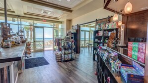 A spacious store with wooden flooring, glass doors leading to a balcony with a view of the ocean, shelves stocked with various items, and hanging pendant lights. - 2 Bedrooms in Aqua Resort - Remodeled with amazing views! Beach chairs included! (Panama City Beach)