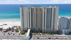 A high-rise hotel with multiple balconies, a parking lot, and a beach view. - 2 Bedrooms in Aqua Resort - Remodeled with amazing views! Beach chairs included! (Panama City Beach)