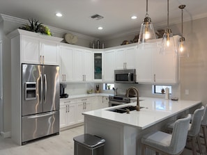 A modern kitchen with white cabinetry, stainless steel appliances, and a central island with bar stools.