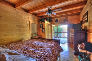 Quarto de cabana de madeira com cama, ventilador de teto e vista para um deck externo.