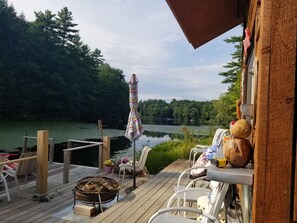 A wooden deck with outdoor seating, a fire pit, and a view of a lake surrounded by trees. - adirondack style all season lodge/resort on a natural glacier pond- SPECIAL RATE (Granville)