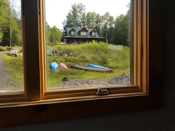 Vista desde la ventana de una cabaña con un patio cubierto de césped, un canoa y un kayak.