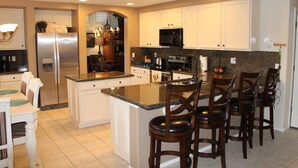 A spacious kitchen with white cabinets, a stainless steel refrigerator, a granite countertop, and a bar area with four stools. - Beautiful Desert Escape w/private pool just north of Scottsdale. Special rates!  (Cave Creek)