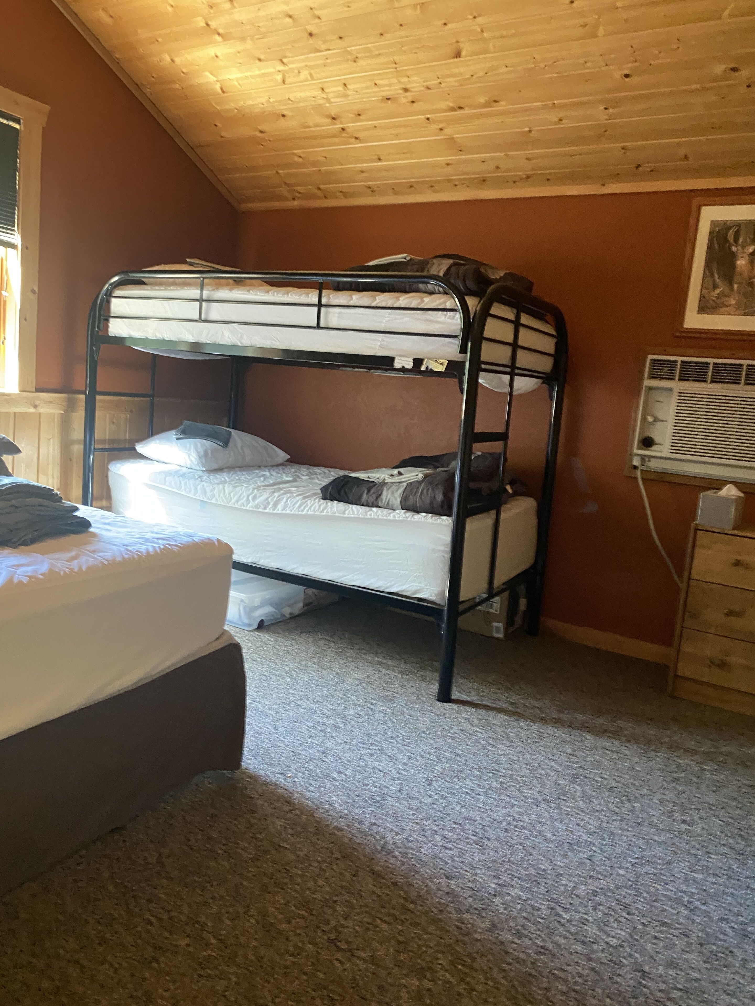 A bunk bed room with a wooden ceiling, a radiator, and a window.