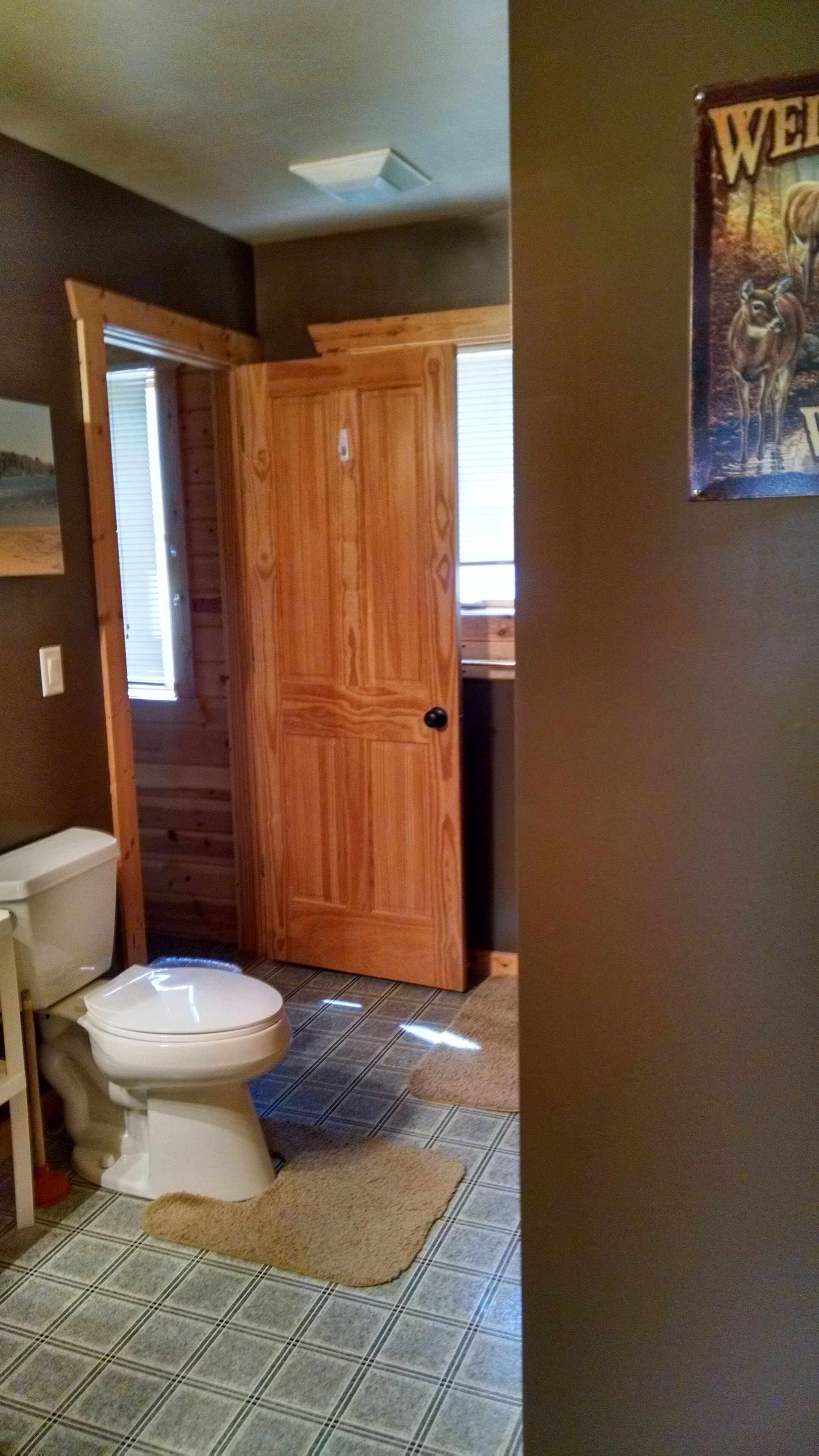 Une salle de bain avec une porte en bois, des toilettes et une affiche accrochée au mur.