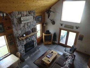 A cozy lodge interior with a stone fireplace, wooden walls, and a stone wall adorned with hunting trophies. - Taking summer rentals! (La Pointe)