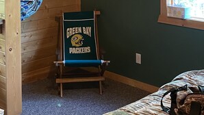 Una habitación con literas, una ventana con vistas, un cuadro en la pared y una silla con un cartel de los 'Green Bay Packers'.
