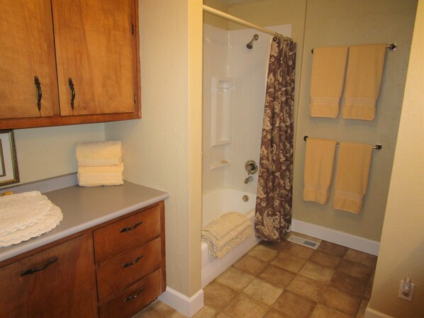 Une salle de bain avec un meuble-lavabo en bois, une douche avec un rideau à motifs et plusieurs serviettes accrochées au mur.