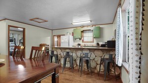 A kitchen with wooden chairs, a dining table, and a counter with green cabinets. - The Magnolia — A River-View Bungalow with Hot Tub (Pencil Bluff)