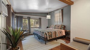 A bedroom with a bed, a potted plant, a window, and a ceiling light fixture. - The Magnolia — A River-View Bungalow with Hot Tub (Pencil Bluff)