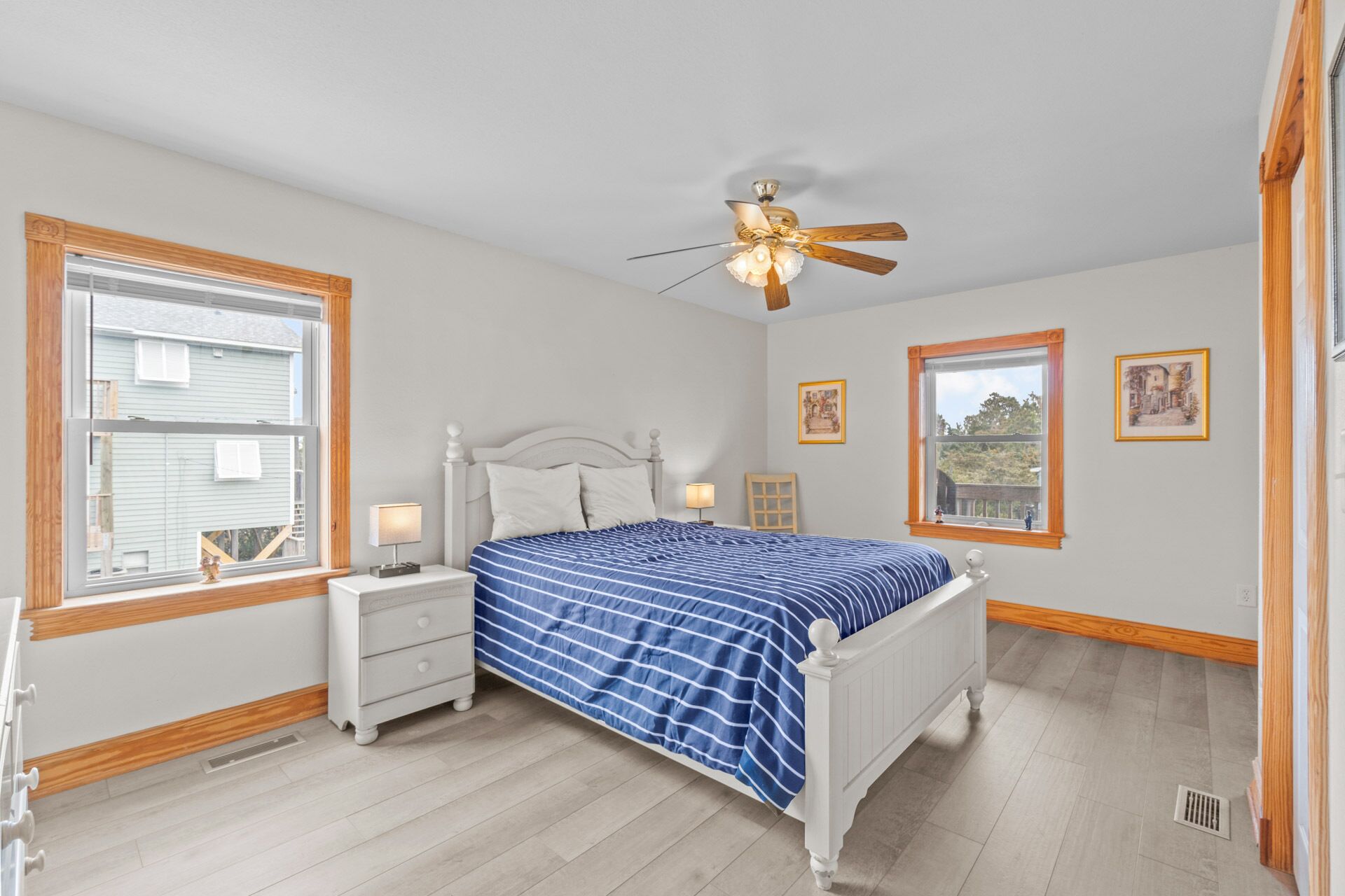 A bedroom with a bed, nightstands, a ceiling fan, and two windows.