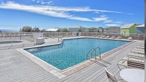 Un espace piscine doté d’une terrasse en bois, de chaises longues et offrant une vue dégagée sur l’océan.