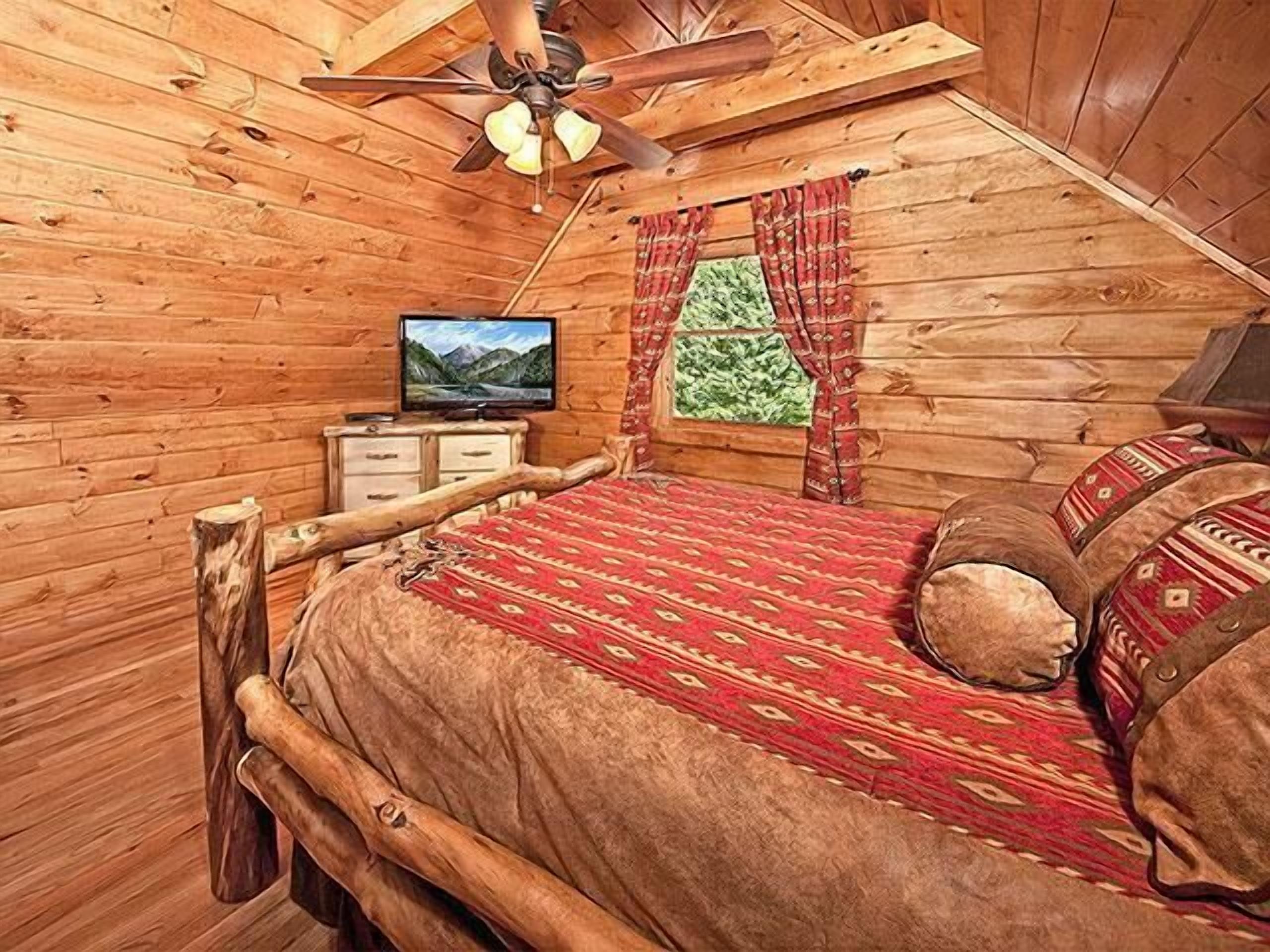Camera da letto accogliente in legno con un letto, una televisione e una finestra con tende.