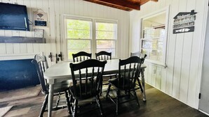 A dining area with a wooden table and chairs, a window with a view of greenery, and a sign reading "Welcome to the Lake House".