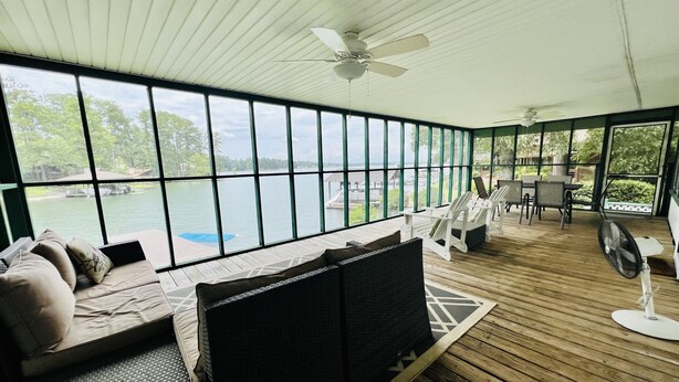 A covered outdoor seating area with a view of a lake, wooden flooring, and ceiling fans.