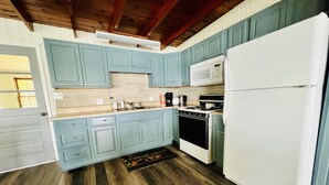 A kitchen with light blue cabinets, a white refrigerator, a stove, and a microwave.