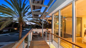 A balcony with a wooden floor, a palm tree, and a glass wall overlooking a street.