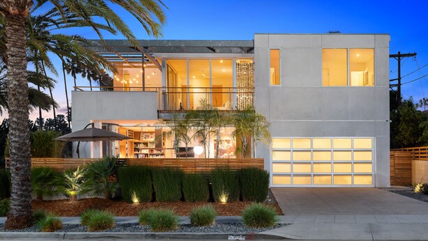 A modern two-story house with a large garage, a balcony, and a well-lit entrance.