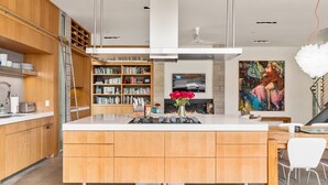 A modern kitchen with wooden cabinets, a central island, and a dining area with white chairs.