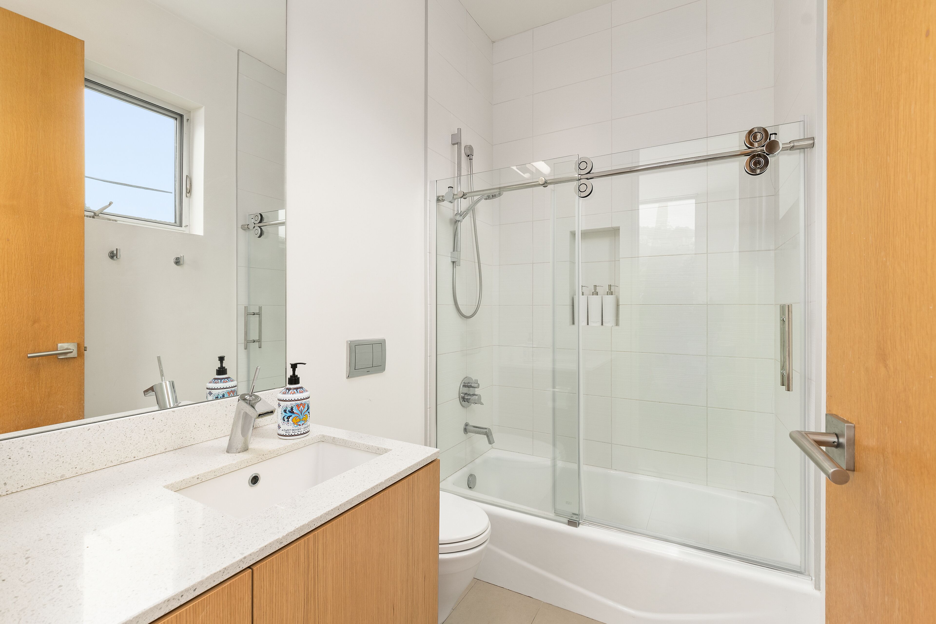 A modern bathroom with a glass-enclosed shower, a white sink, and a wooden vanity.