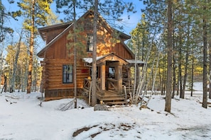 A log cabin with a porch, surrounded by trees and snow. - The Outback- Log Cabin with Access to Pool! (Lead)