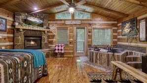 A cozy cabin interior with a stone fireplace, a bed with a quilt, a bench, a hot tub, and a ceiling fan. - Secluded Studio Cabin Rental-Honeymoon/Anniversary Getaway-dog Friendly (Pigeon Forge)