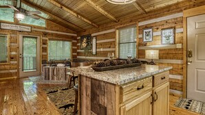 A wooden cabin interior with a kitchen island, wooden walls, and a ceiling fan. - Secluded Studio Cabin Rental-Honeymoon/Anniversary Getaway-dog Friendly (Pigeon Forge)