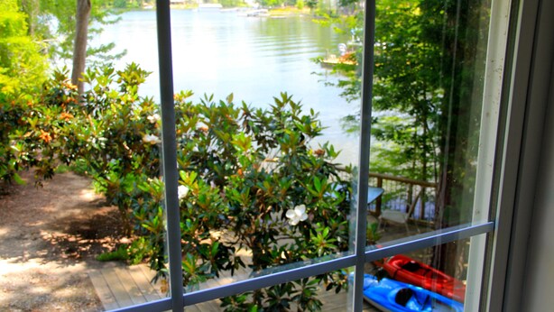 Blick durch ein Fenster auf einen See mit Kajaks und einer Holzterrasse.