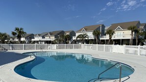 En swimmingpool med ett trädäck runt om, omgiven av ett vitt staket och palmer.