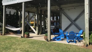 En takförsedd uteplats med träbjälkar, ljusslingor och blå Adirondack-stolar.
