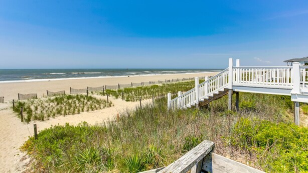 Une promenade en bois qui mène à une plage d’où l’on a une vue dégagée sur l’océan.