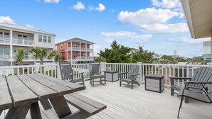 Une terrasse en bois avec des tables et des chaises pour pique-niquer, une clôture blanche et des bâtiments en arrière-plan.