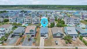 Un quartier résidentiel situé sur la côte, composé de plusieurs maisons à deux étages, doté d’une piscine centrale et offrant une vue sur l’océan.