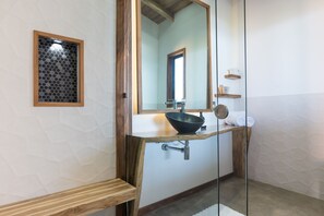 Ein Badezimmer mit einem Holzbadezimmerhocker, einem schwarzen Waschbecken, einem Spiegel und einem Holzregal mit Handtüchern.