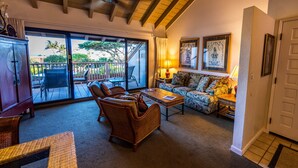A spacious living area with a sofa, chairs, and a coffee table. A sliding glass door leads to an outdoor patio with a table and chairs. - Beautiful 2 Bedroom Oceanview Condo at Maui Kamaole The Perfect Maui Escape! (Kihei)
