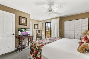 A hotel room with a bed, a television, a ceiling fan, a desk, and a view of the outdoors.