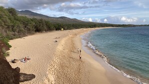 A wide sandy beach with gentle waves, a few people walking, and a mountainous backdrop. - Beautiful 2 Bedroom Oceanview Condo at Maui Kamaole The Perfect Maui Escape! (Kihei)