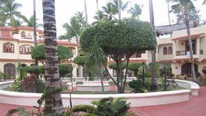 A courtyard with palm trees, a central fountain, and buildings with red-tiled roofs.