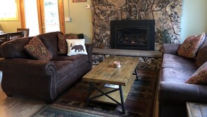 A cozy living room with a stone fireplace, leather sofas, and a coffee table. -  5-Star Tahoe Chalet with Hot Tub in Quiet Setting (South Lake Tahoe)