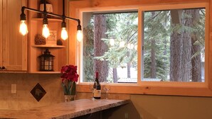 A kitchen with a stone countertop, wooden cabinets, a window with a view of trees, and a hanging light fixture. -  5-Star Tahoe Chalet with Hot Tub in Quiet Setting (South Lake Tahoe)