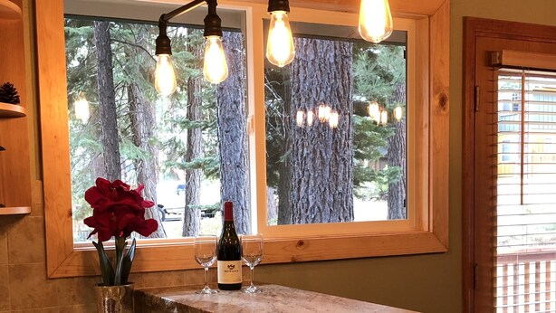 A kitchen with a granite countertop, a vase with a red flower, a bottle of wine, and a window with a view of trees. -  5-Star Tahoe Chalet with Hot Tub in Quiet Setting (South Lake Tahoe)