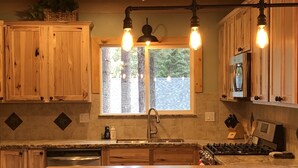 A kitchen with wooden cabinets, a granite countertop, a stainless steel sink, and a window with a view of trees. -  5-Star Tahoe Chalet with Hot Tub in Quiet Setting (South Lake Tahoe)