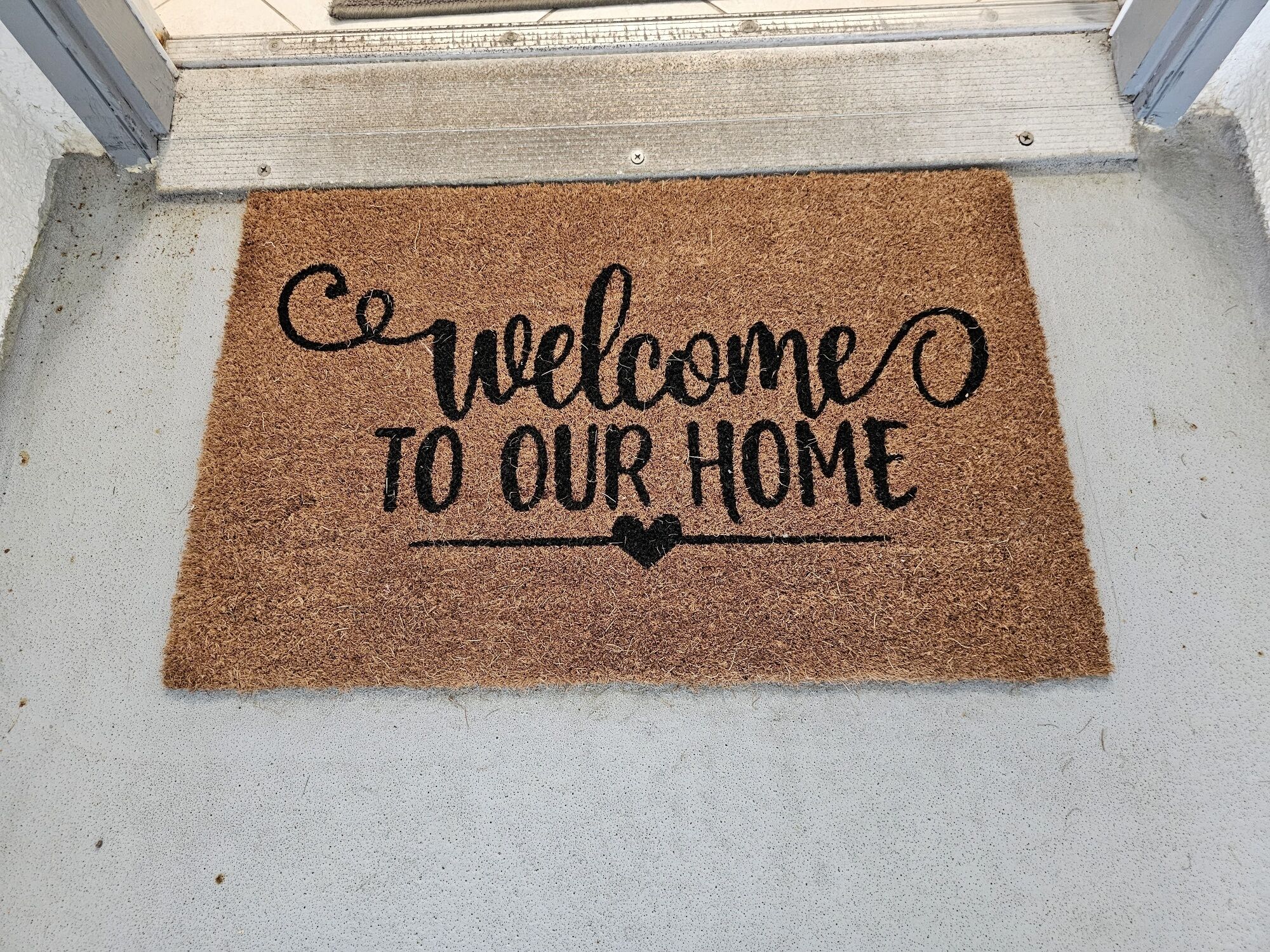 Alfombra de bienvenida con el texto 'bienvenidos a nuestro hogar' sobre una superficie texturizada.